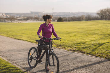 Mature woman standing with bicycle on sunny day - JCCMF09336