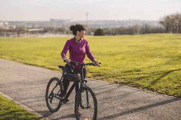Reife Frau stehend mit Fahrrad an einem sonnigen Tag - JCCMF09336