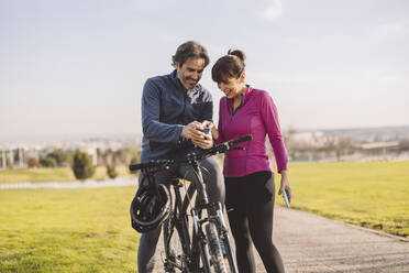 Glückliches reifes Paar mit Fahrrad und Smartphone im Park - JCCMF09338