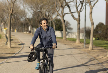 Happy mature man riding bicycle on road - JCCMF09340