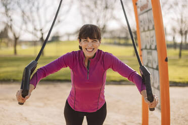 Glückliche Frau bei der Arbeit an einem Fitnessgerät im Park - JCCMF09342