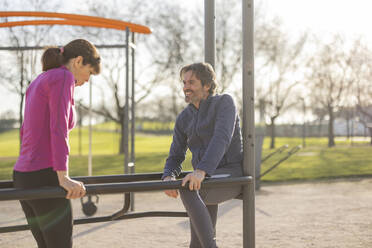Mature couple exercising on parallel bars in park - JCCMF09344