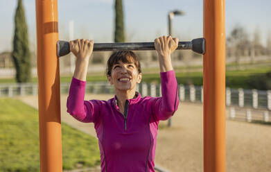 Happy woman exercising with horizontal bar in park - JCCMF09345