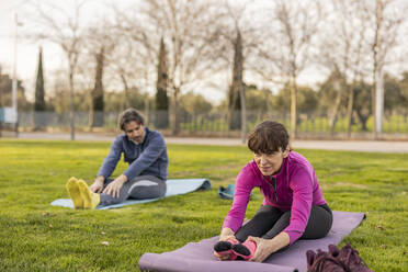 Lächelnde Frau mit Mann beim Yoga im Park - JCCMF09351