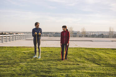 Älteres Paar beim Training mit Widerstandsbändern im Park an einem sonnigen Tag - JCCMF09367