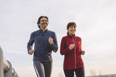 Happy mature man and woman running together - JCCMF09379