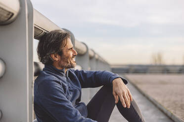 Happy mature man sitting by railing - JCCMF09381