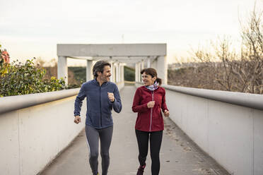 Happy mature couple jogging on bridge - JCCMF09399
