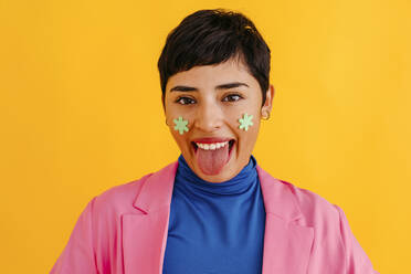 Junge Frau streckt Zunge vor gelbem Hintergrund heraus - TCEF02245