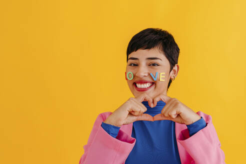 Woman making heart shape gesture against yellow background - TCEF02250