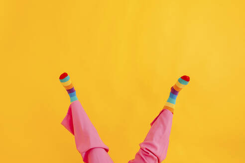 Feet of woman wearing multi colored socks against yellow background - TCEF02262