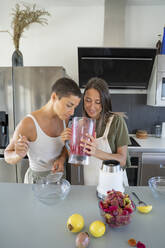 Woman holding blender with prickly pears juice by friend in kitchen at home - FBAF02060