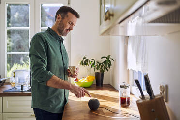 Mann, der zu Hause steht und eine Kaffeetasse hält, schaltet einen Lautsprecher ein - BSZF02155