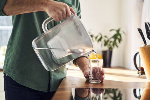 Man pouring water from a filter jug into a glass in the kitchen, close up - BSZF02170