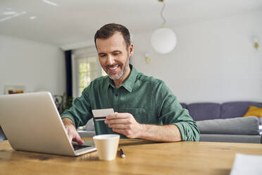Mann zahlt mit Kreditkarte auf seinem Laptop am Schreibtisch sitzend - BSZF02186