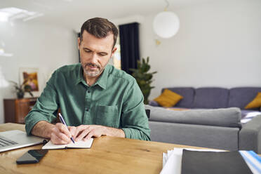 Hübscher Mann arbeitet von zu Hause aus und macht sich Notizen am Schreibtisch - BSZF02207