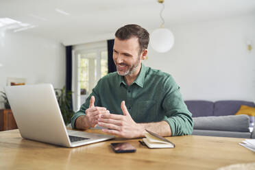 Cheerful man having video call sitting at desk at home - BSZF02209