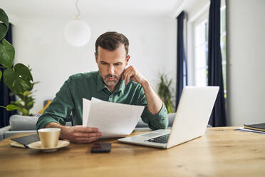 Worried businessman doing paperwork sitting at table working from home - BSZF02227