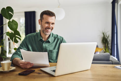 Confident businessman doing paperwork sitting at table working from home - BSZF02229