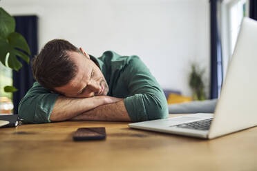 Überarbeiteter Mann schläft auf den Armen am Schreibtisch - BSZF02235