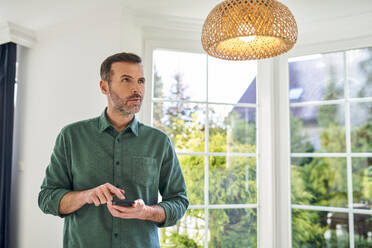 Erwachsener Mann steuert Lampe mit Smartphone zu Hause - BSZF02252