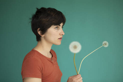 Thoughtful woman holding dandelions against green background - AXHF00254
