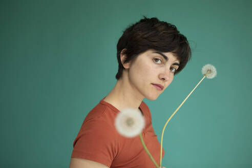 Woman with short hair holding dandelions against green background - AXHF00255