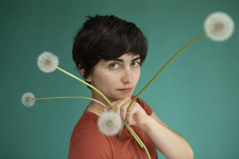 Young woman with dandelions against green background - AXHF00257
