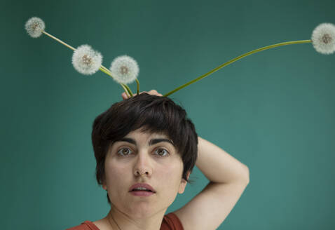 Woman holding dandelions behind head against green background - AXHF00260