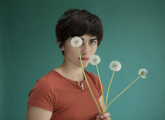 Woman covering eye with dandelion against green background - AXHF00261