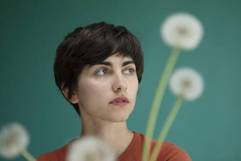 Contemplative woman with dandelions against green background - AXHF00263