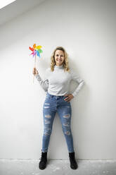 Woman with hand on hip holding pinwheel toy standing in front of wall - HMEF01509