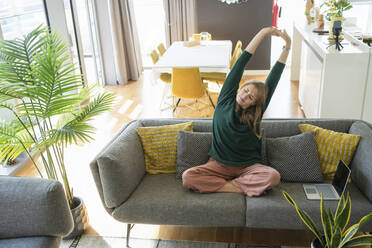 Woman stretching arms on sofa at home - SVKF01237