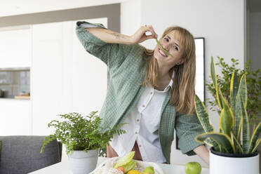 Glückliche Frau macht Schnurrbart aus grünen Bohnen im Gesicht zu Hause - SVKF01252