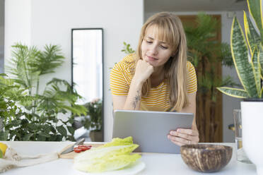 Woman with hand on chin watching tutorial through tablet PC - SVKF01256