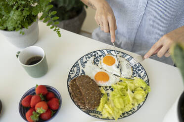 Hands of woman cutting fried egg with knife at home - SVKF01270