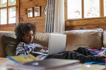 Boy using laptop resting on sofa at home - LJF02492