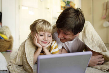 Smiling father with daughter watching tablet PC lying on floor at home - TYF00740