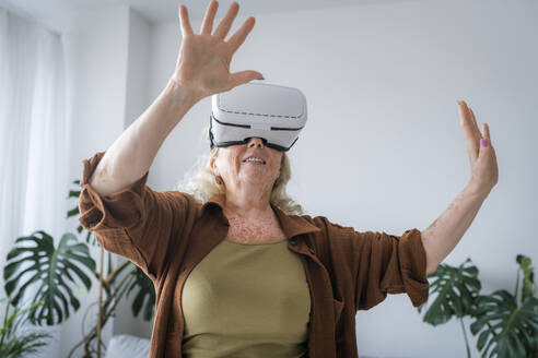Ältere Frau mit Vitiligo-Haut trägt zu Hause ein Virtual-Reality-Headset - AAZF00010