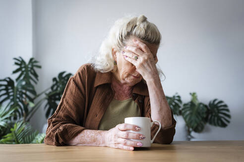 Depressive ältere Frau mit Tasse auf dem Tisch zu Hause - AAZF00021