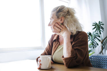 Einsame ältere Frau mit Tasse sitzt am Tisch zu Hause - AAZF00022