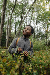 Lächelnder Junge, der in den Ferien in der Nähe von Pflanzen im Wald steht und träumt - MASF34660