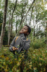 Junge schaut nach oben und isst Beeren in der Nähe von Pflanzen im Wald - MASF34661