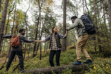 Glückliche Frau hilft Mann und Sohn beim Spaziergang auf einem Baumstamm im Wald - MASF34664