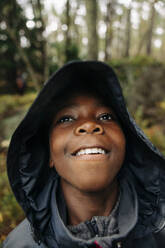 Thoughtful boy looking away wearing raincoat in forest - MASF34674