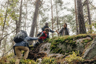 Familie hilft Vater beim Klettern während einer Wanderung im Wald - MASF34685