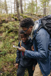Vater benutzt Smartphone mit Sohn bei der Erkundung des Waldes im Urlaub - MASF34686