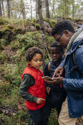 Father showing smart phone to sons while hiking in forest - MASF34687