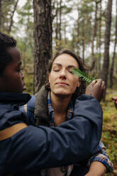 Son touching leaf on mother's eye in forest - MASF34701