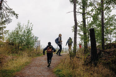 Rear view of son running towards mother on trail while hiking in forest - MASF34705